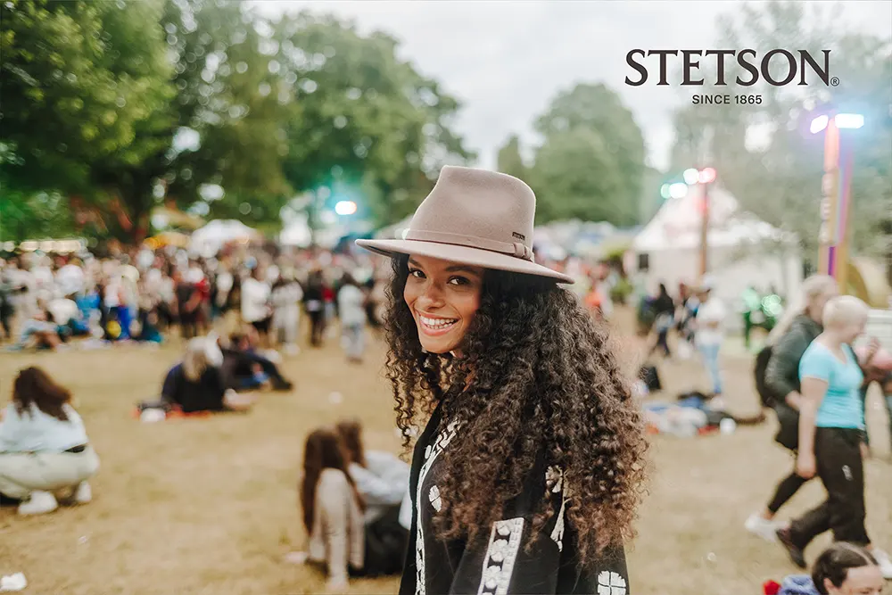 Damenhut von Stetson – Sommerlicher Auftritt mit Fedora-Look Frau mit braunem Stetson-Fedora-Hut lächelt auf einem Open-Air-Festival