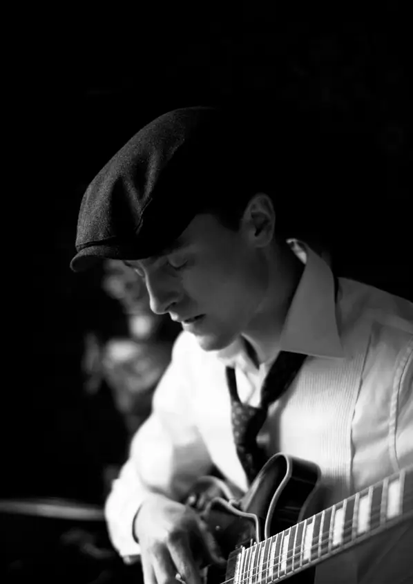 Wigens Schiebermütze im Jazzstil Mann mit eleganter Wigens Schiebermütze spielt Gitarre – stilvoller Look im Schwarzweiß-Porträt
